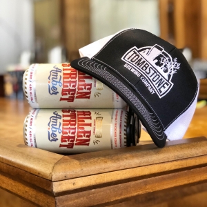 tombstone brewery hat on top of 4 pack of beer